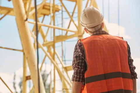 A construction engineer in an orange vest and hard hat stands with his back t Foto stock