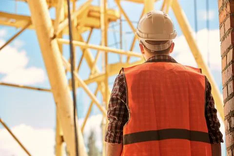 A construction engineer in an orange vest and hard hat stands with his back t Foto stock