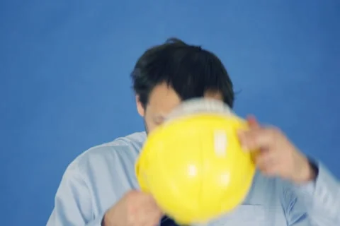 Construction engineer putting on yellow helmet, on blue background NTSC Stock-Footage 2842814