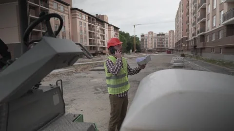 Construction engineer in safety vest and helmet talks on phone while examining Stock Footage 323880323