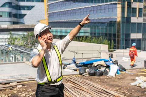 A construction engineer talks on his phone while pointing toward the site, .. Stock Photos
