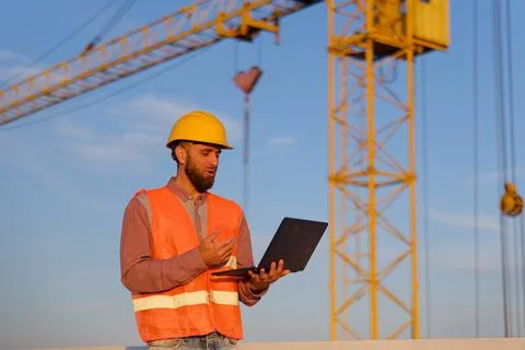 Construction engineer using laptop at building site with crane in background Stockfoto's