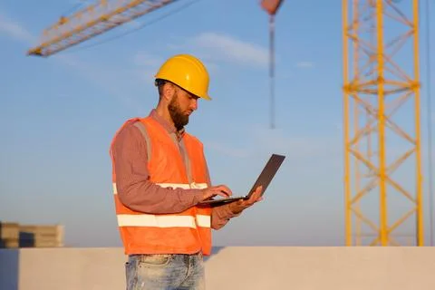 Construction engineer using laptop at building site with crane in background Stockfoto's