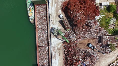 Construction equipment and cranes work at a scrap metal yard next to a body of Stock-Footage 337911757