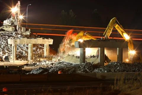 Construction equipment demolishing bridge at night Stock Photos