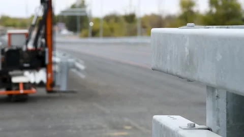 Construction equipment installs or adjusts a metal barrier along the road. Stock Footage 329869010