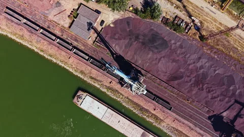 Construction equipment loads materials on a barge near a river bank in an Stock Footage 344233203
