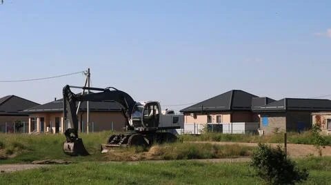 A construction excavator against the backdrop of new cottages Stock Photos