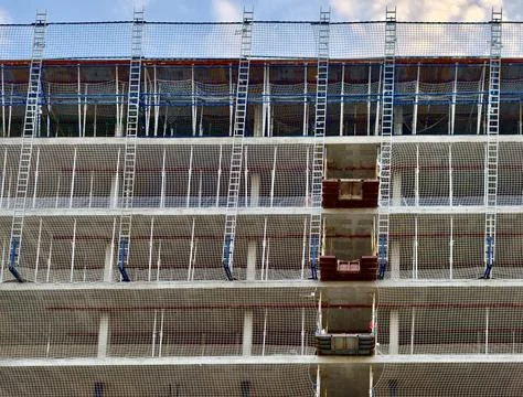 Construction facade with safety nets, ladders, scaffolding, and suspended d.. Stock Photos