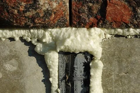 Construction foam is yellowish on a grayscale cement wall under red granite.. Stock Photos