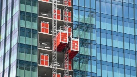 Construction hoists moving along glass high rise facade downtown Stock Footage 331225761