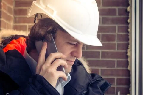 Construction inspector in white helmet talking on mobile phone on the brown Stock Photos