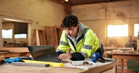 Construction, laptop and typing with man in carpentry workshop for lumber or Stock Photos