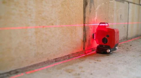The construction laser level is on the floor. The beam is directed at the wal Foto stock
