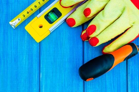 Construction level, gloves and roulette on wooden blue background. Stock Photos