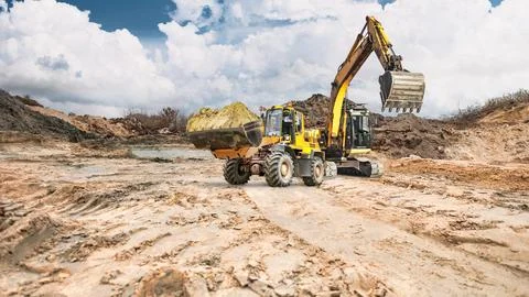 A construction loader moves soil, while in the background an excavator with.. Photos