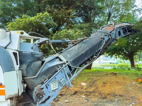 Construction machine performing work at a site near green trees on a sunny da Stock Photos