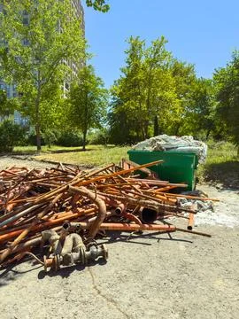 Construction materials are stacked on the ground near a green dumpster in a p Stock Photos