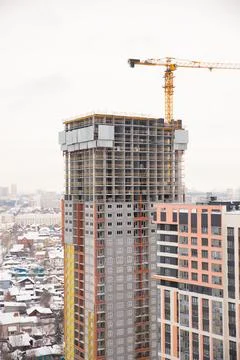 Construction of a modern high-rise building with crane in a snowy city Stock Photos
