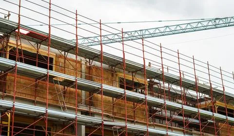 Construction of a new brick building using red scaffolding and a tower crane Stock Photos