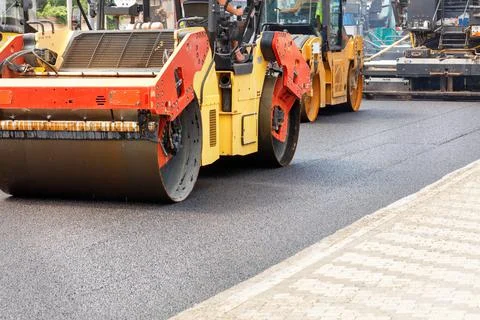Construction of a new road, road rollers compacting fresh asphalt on the road Stock Photos