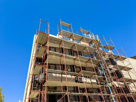 Construction project of a building with scaffolding under clear blue sky Stock Photos