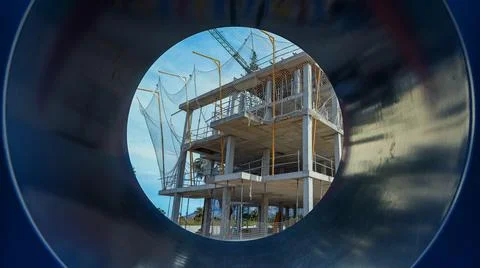 Construction project viewed through a pipe at a building site under clear sky Stock Photos