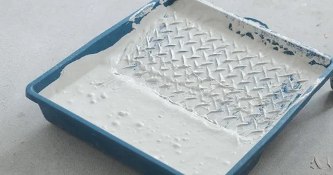 Construction roller is lowered into paint tray with white paint. Blue ditch Stock Footage 129837320