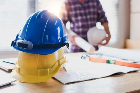 Construction safety helmets on table with engineer holding blueprint backgrou Stock Photos