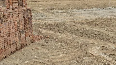 A construction scene with a large pile of red-orange bricks stacked on the .. Stockfoto's
