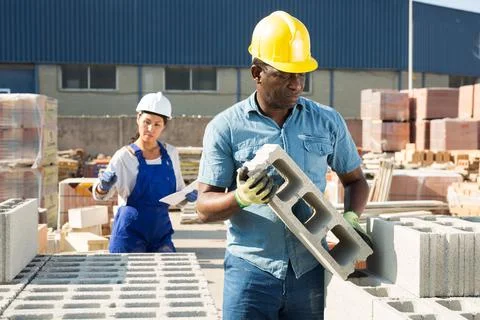 Construction shop worker stacks bricks on an open air site at summer day Stockfoto's