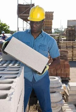 Construction shop worker stacks bricks on an open air site at summer day Stockfoto's
