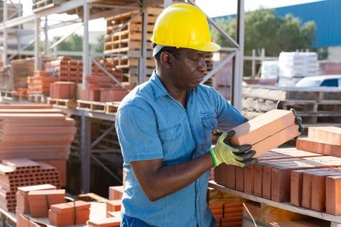 Construction shop worker stacks bricks on an open air site at summer day Stockfoto's