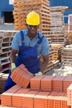 Construction shop worker stacks bricks on an open air site at summer day Stock Photos
