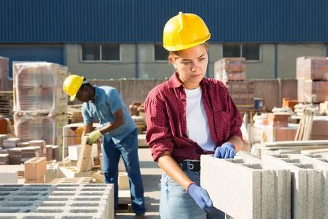 Construction shop worker stacks bricks on an open-air site Stockfoto's