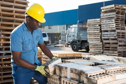 Construction shop worker stacks bricks on an open air site at summer day Stock Photos