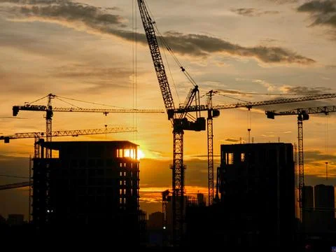 Construction site and tower cranes against the backdrop of a bright sunset Stock Photos