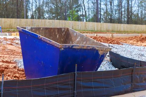 Construction site blue dumpster filled with dirt near gravel path Stock Photos