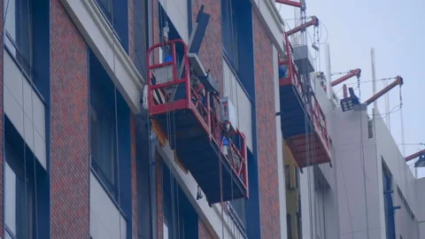 At a construction site, builders in cradle on cables fastens cladding panels Stock Footage 229836973
