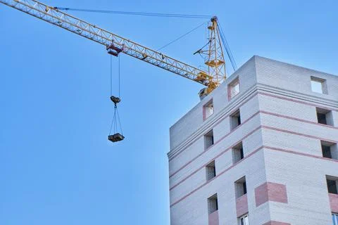 Construction site. Crane and multi-storey brick house against the blue sky. Stock Photos