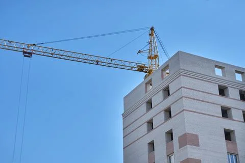 Construction site. Crane and multi-storey brick house against the blue sky. Stock Photos