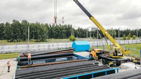 Construction Site with Crane Lifting Pipes and Workers Present Stock Photos