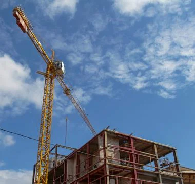 Construction site with crane operating under blue sky on a sunny day Stock Photos