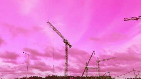 Construction site with cranes under a pink sky during sunset near a city locatio Stock Footage 323845274