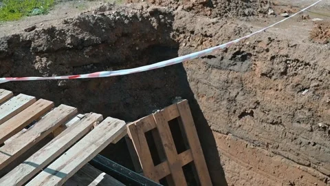 A construction site displays a deep trench surrounded by caution tape and wooden Stock Footage 338446988