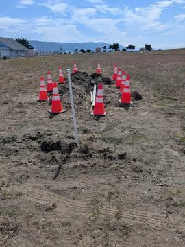 Construction site with exposed pipe in a dug field surrounded by orange cones Stockfoto's