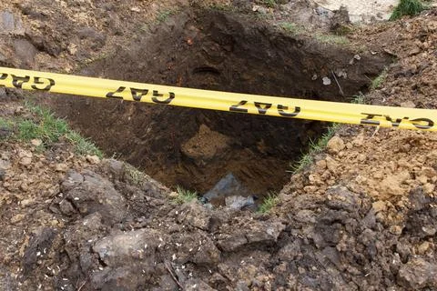 Construction site gas line warning tape across deep excavation hole in ground Stock Photos