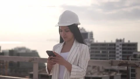 Construction site in helmet holds mobile phone and rolled-up paper plan Stock Footage 240302811