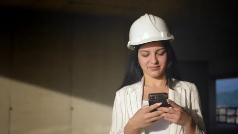 Construction site in helmet holds mobile phone and rolled-up paper plan Vídeos de archivo 240336188