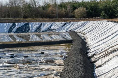 Construction Site With Large Pond Covered in Tarps and Gravel Near Trees in.. Foto stock